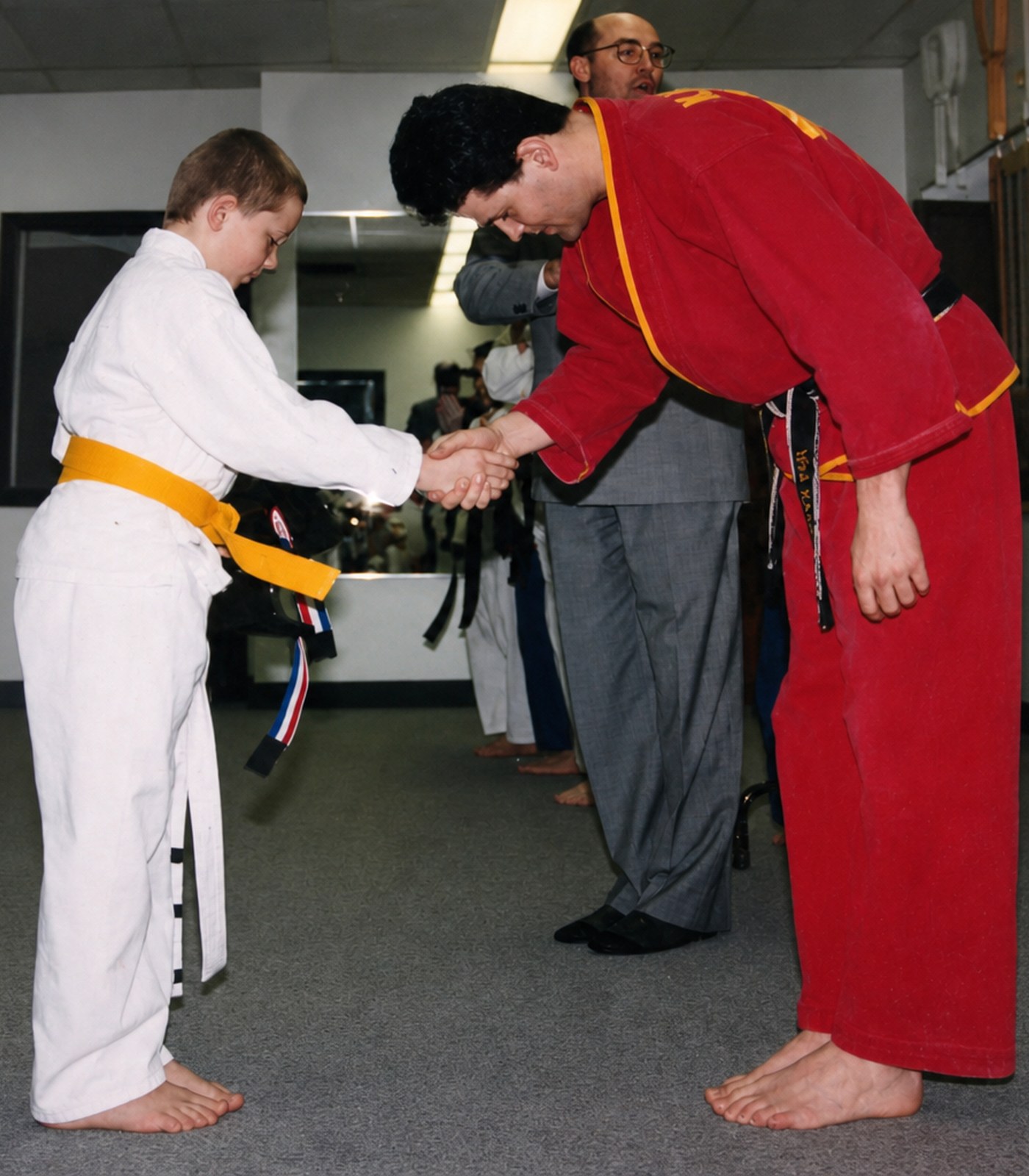 A gold-belt student shaking hands with an instructor during a promotion
